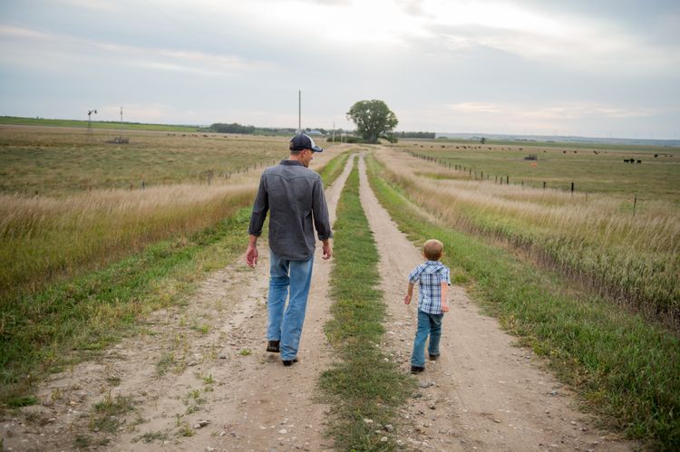 A father and his son inspect their land while walking along a dirt road.